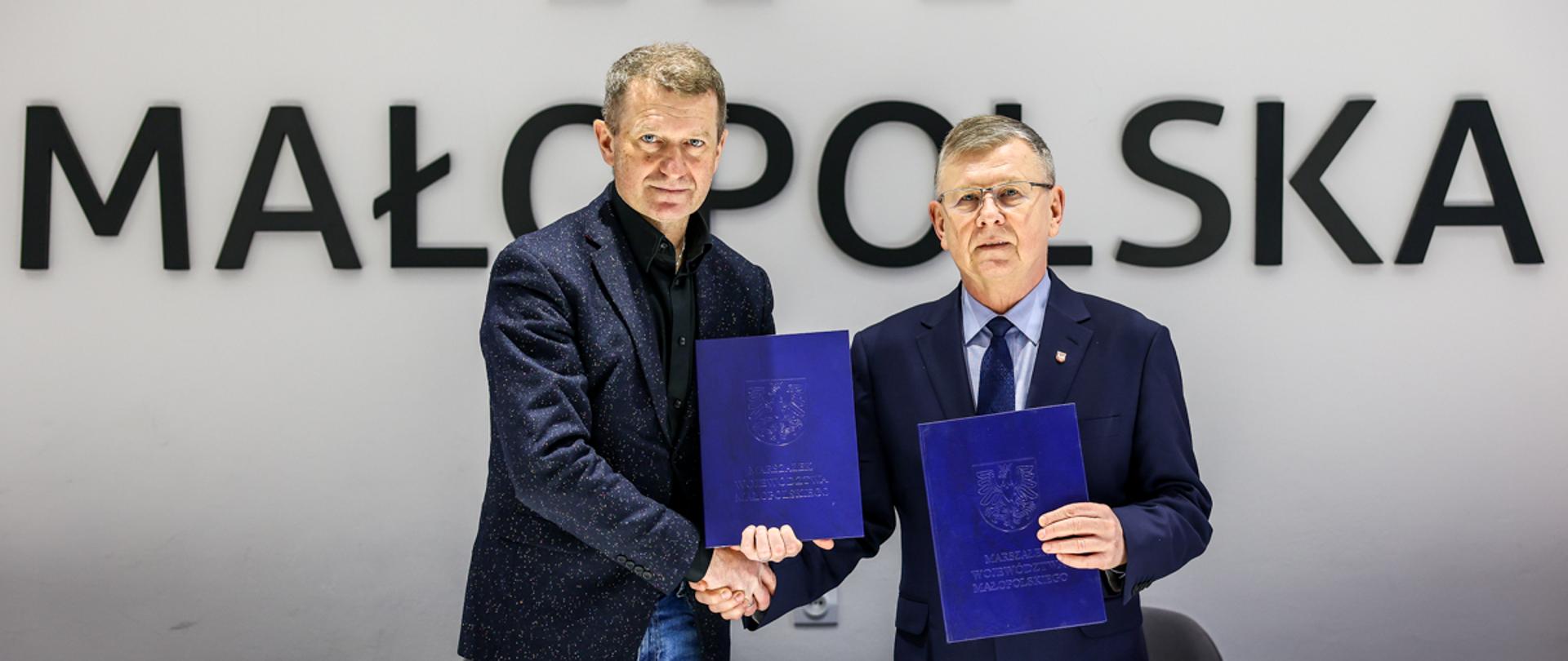 Ireneusz Raś i wicemarszałek województwa małopolskiego Witold Kozłowski na tle loga województwa