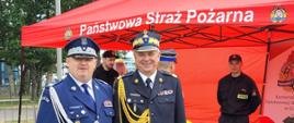 Pomorski komendant wojewódzki Państwowej Straży Pożarnej oraz komendant wojewódzki Policji stoją na tle namiotu strażackiego wraz z wyposażeniem, w namiocie stoją strażacy ubrani w mundury koszarowe.