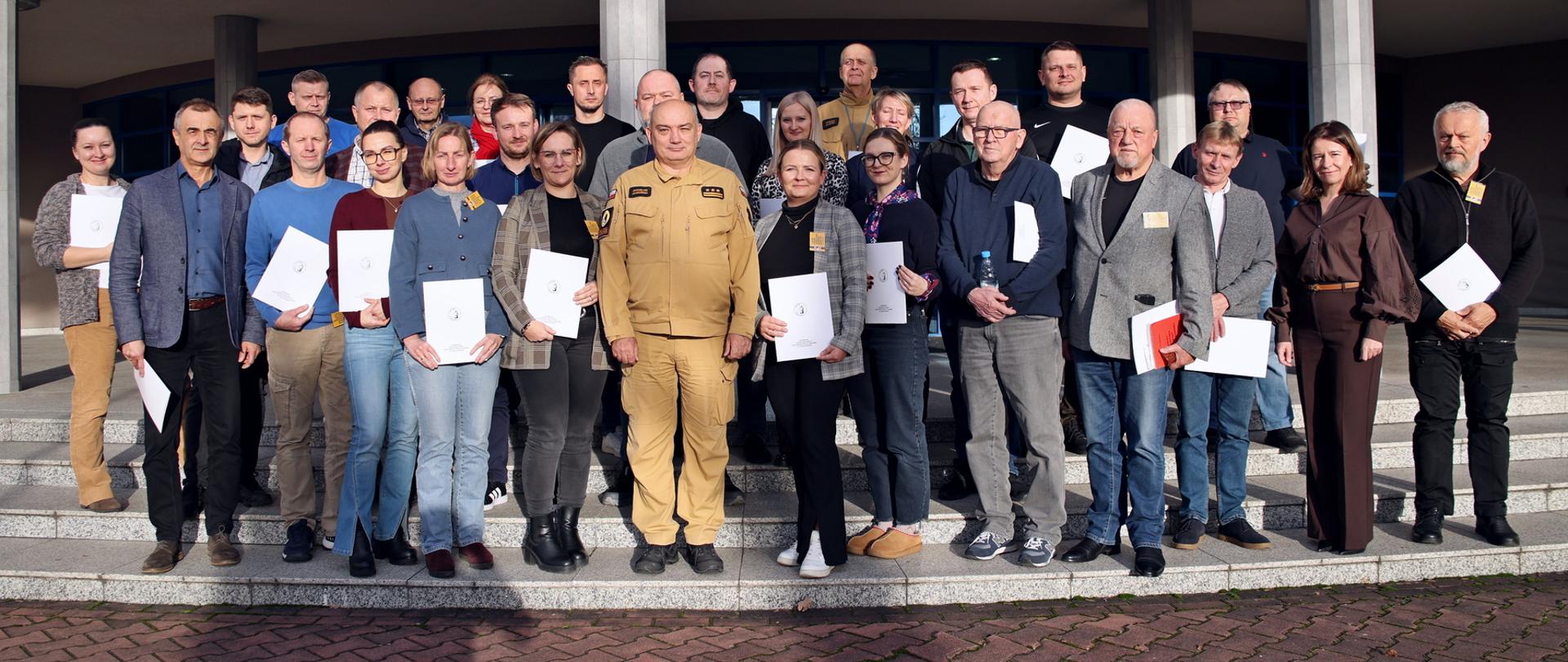 Pamiątkowe zdjęcie grupowe uczestników szkolenia inspektorów ochrony przeciwpożarowej (26 osób) w towarzystwie Komendanta Centralnej Szkoły PSP, kobiety oraz funkcjonariusza CS PSP
