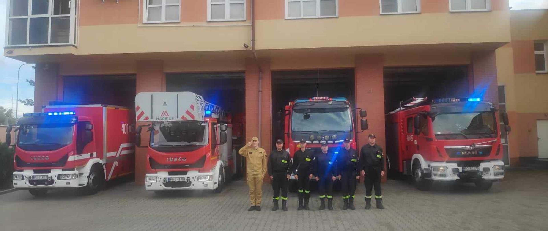 Zdjęcie przedstawia strażaków na placu przed Komendą oddających hołd w 79. rocznicę wybuchu powstania warszawskiego.
W tle samochody strażackie oraz budynek Jednostki Ratowniczo - Gaśniczej.
