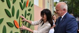 Wojewoda z dyrektor Jelską przyklejają liść do drzewka dobroczyńców 