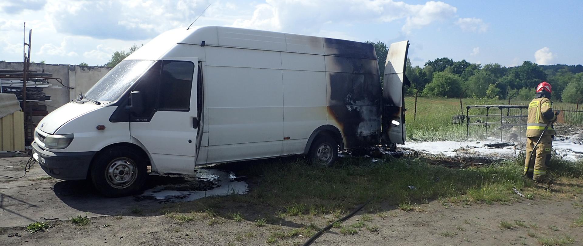Samochód dostawczy ze spaloną tylną częścią, z prawej strony busa strażak podający prąd piany