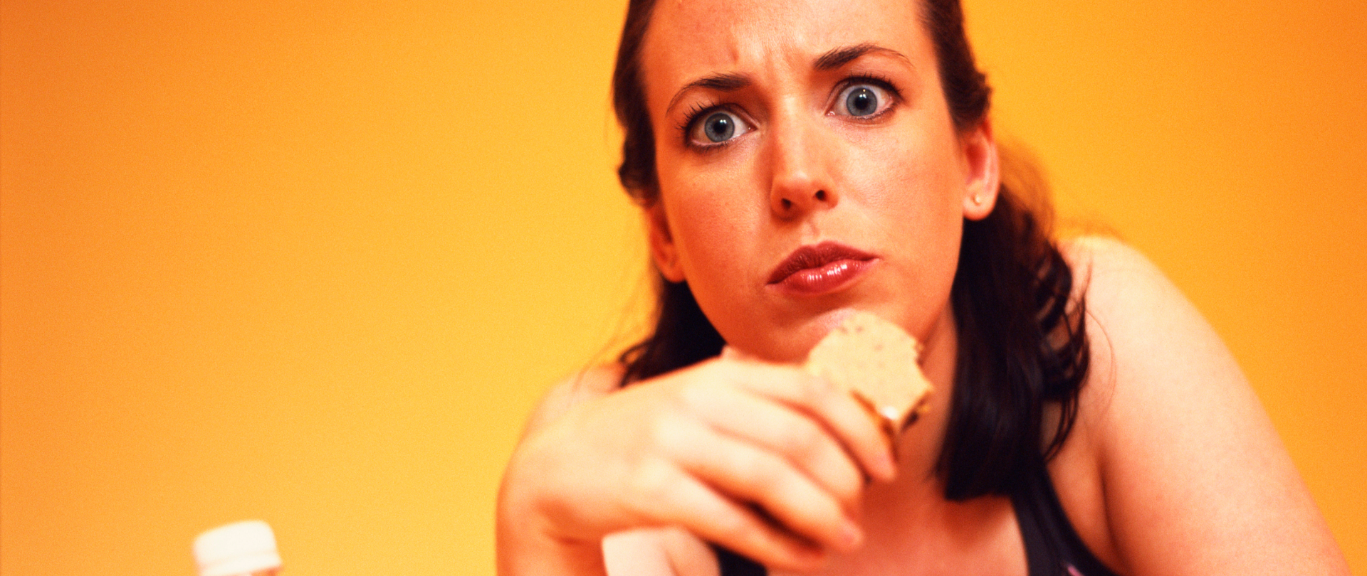 Kobieta z ciastkiem w ręce patrzy zdziwiona.