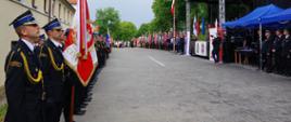 Widok z boku. Po lewej stronie dowódca pododdziału PSP, dalej poczet sztandarowy. Po prawej stronie zasłużeni druhowie OSP , trybuna honorowa, dalej poczty sztandarowe i goście. 
