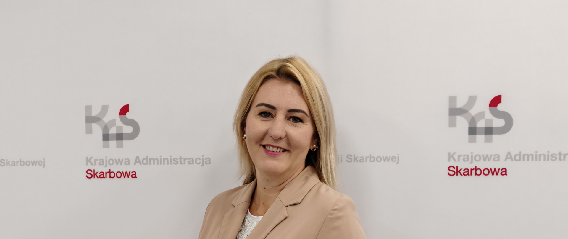 kobieta na tle ściany z logo KAS i napisami Izba Administracji Skarbowej w Bydgoszczy