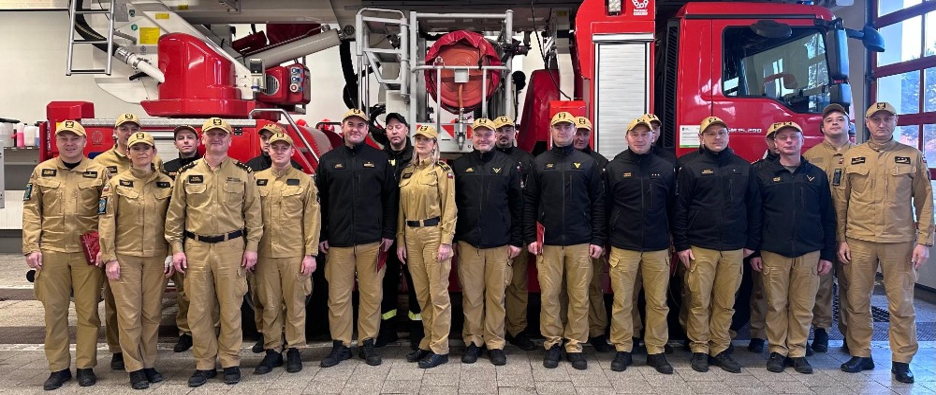 Na zdjęciu znajdują się strażacy ustawieni do zdjęcia na garażu na tle podnośnika