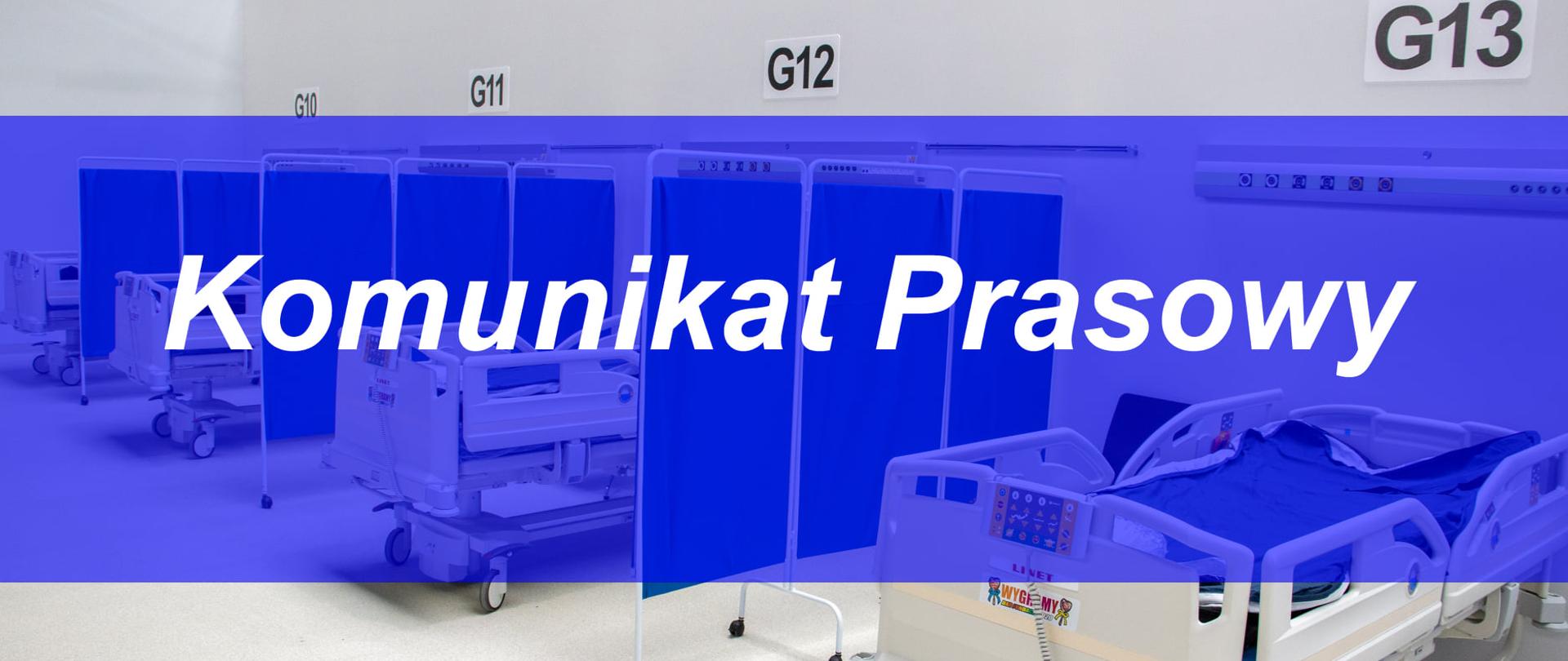 Zdjęcie przedstawia salę szpitalną z trzema łóżkami. Wyposażenie szpitala stanowi tło, na pierwszym planie nieco przeźroczysta granatowa belka na środku zdjęcia z napisem Komunikat Prasowy 