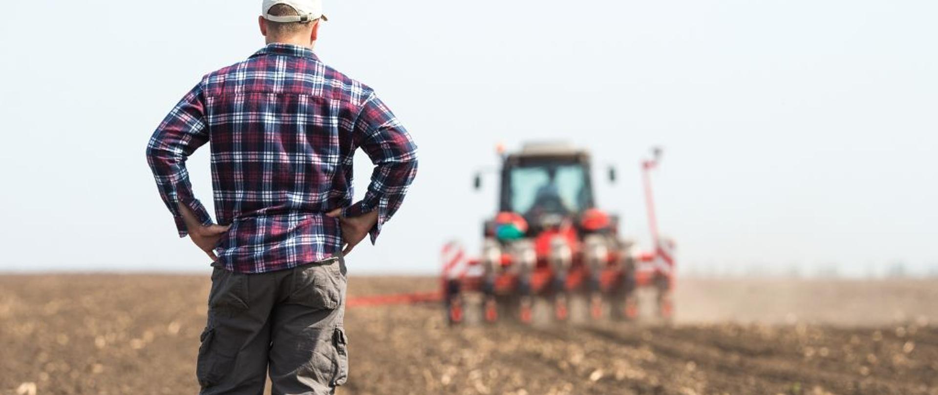 Rolnik obserwuje pracujący w polu ciągnik rolniczy 