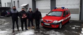 Czterech strażaków na tle samochodu operacyjnego Dacia Logan
