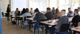 Grupa ludzi siedzi przy ławkach w sali szkoleniowej 
