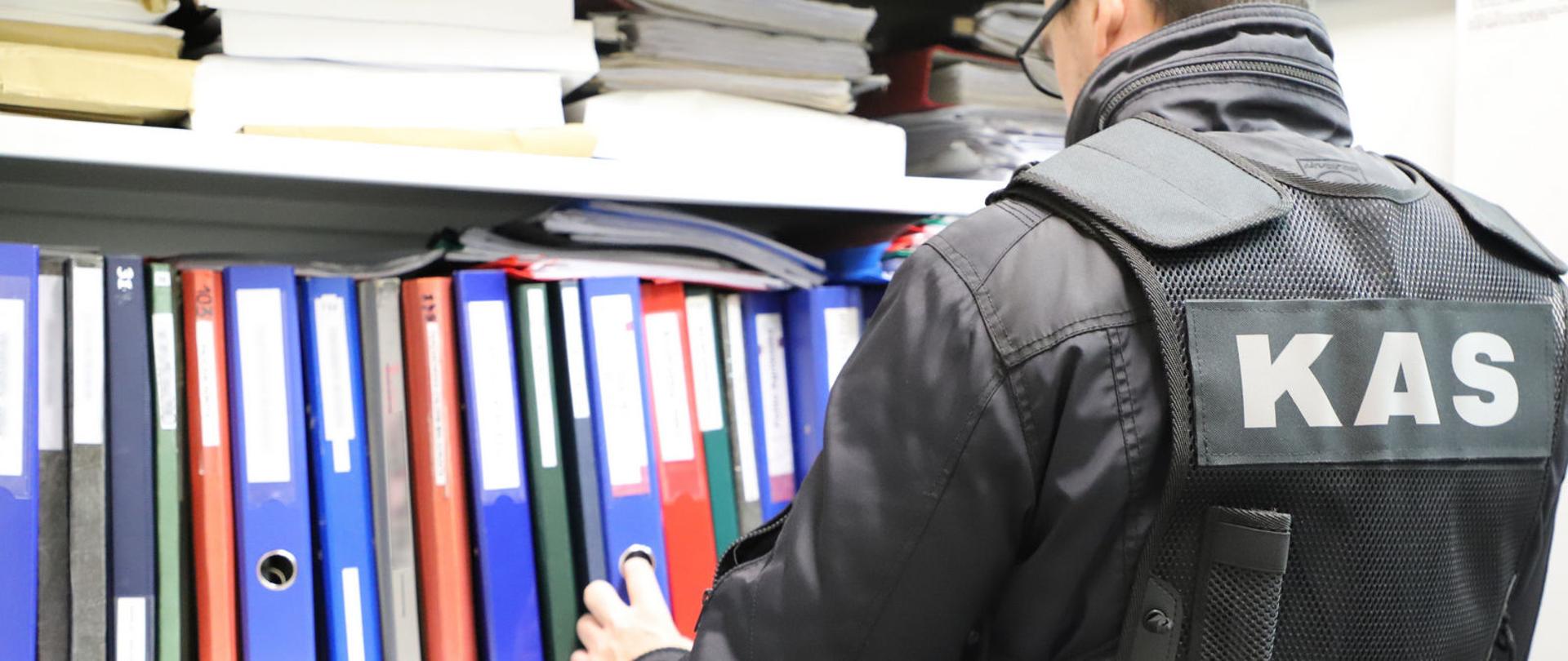 Funkcjonariusz KAS przy szafie z segregatorami z dokumentami, sięga po jeden z segregatorów.