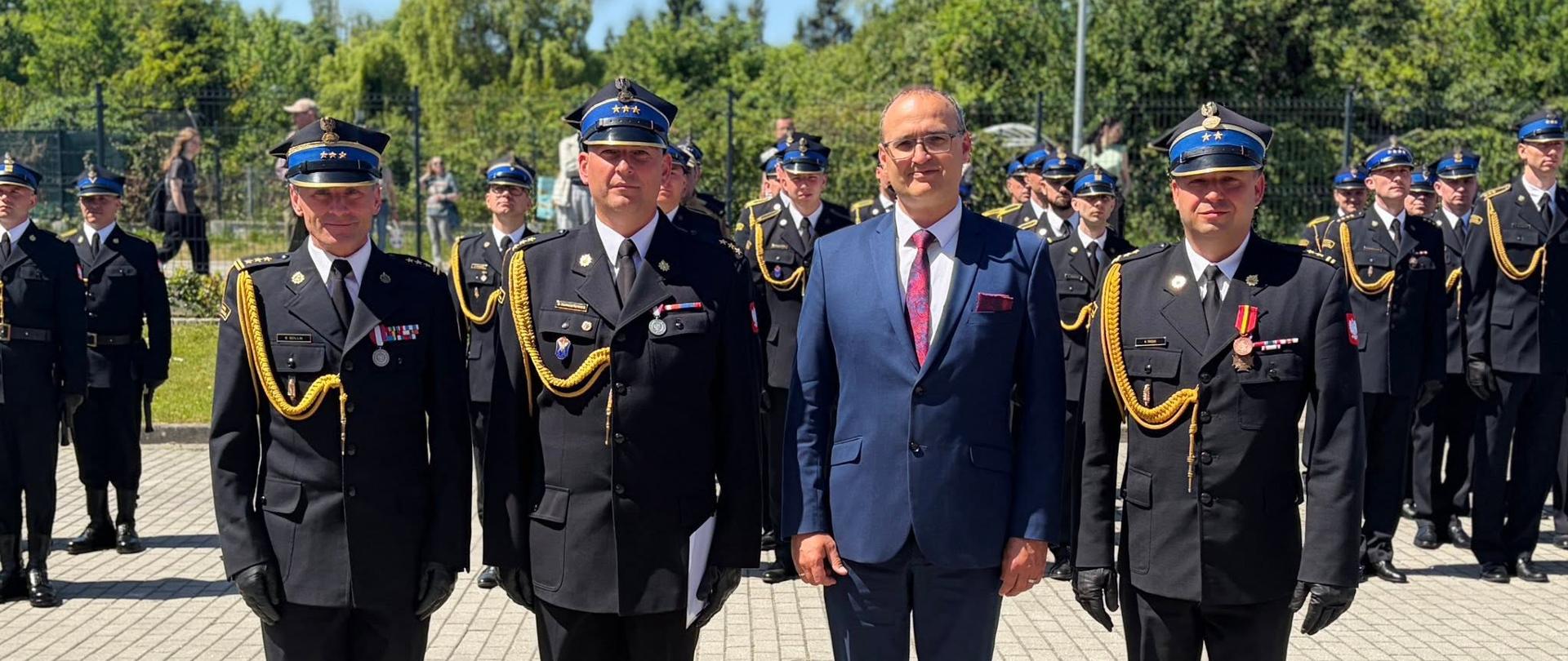 Zdjęcie przedstawia funkcjonariuszy PSP stojących na baczność pośród nich mężczyzna w niebieskim garniturze.