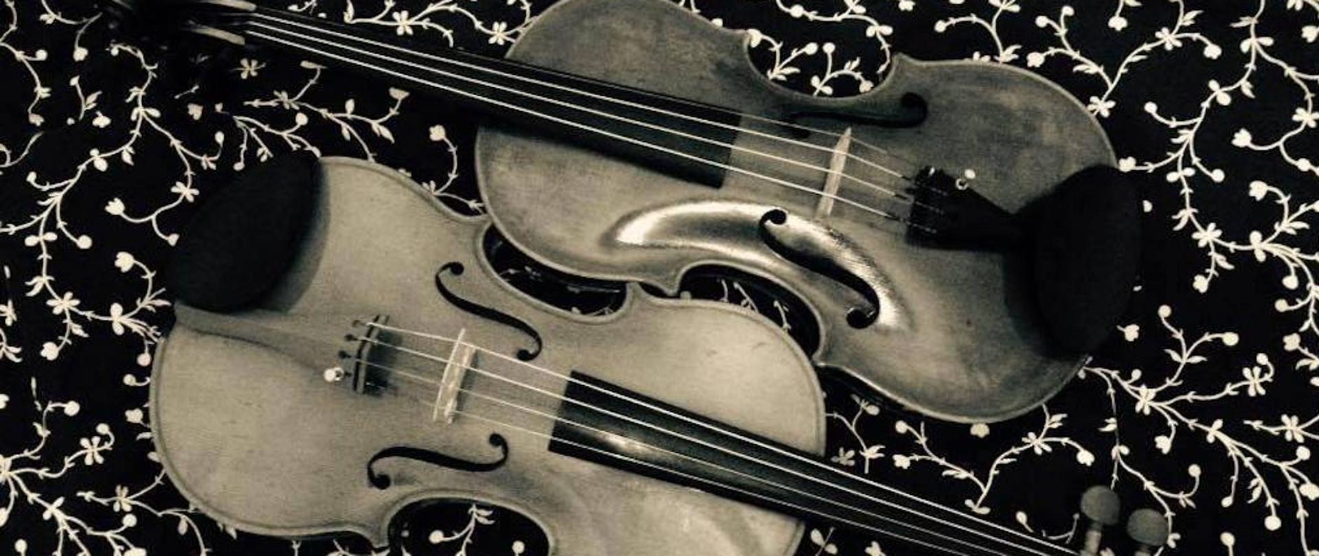 Na czarnym tle z białym wzorem przedstawiono dwoje skrzypiec, które były motywem przewodnim Pruchnickich Konfrontacji Skrzypcowych.