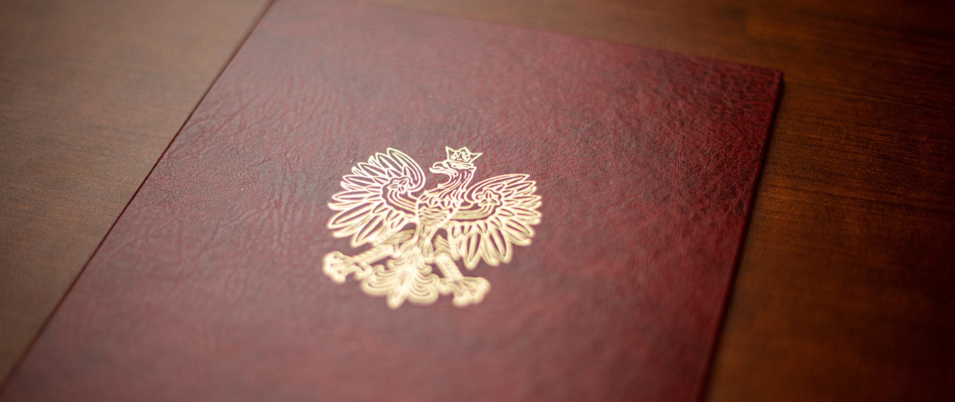Na zdjęciu widać fragment twardej oprawy na dokumenty z wytłoczonym orłem z godła narodowego.