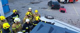 Na placu Komendy Wojewódzkiego Państwowej Straży Pożarnej w Opolu strażacy ochotnicy w ubraniu specjalnym tzw. bojowym zapoznają się budową samochodów w ramach działań ratownictwa technicznego (działania w ramach szkolenia dowódców OSP).