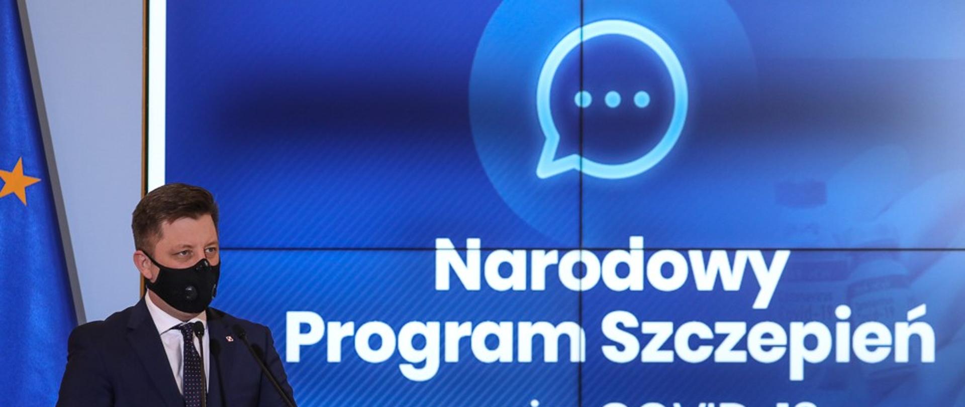 Minister Michał Dworczyk na niebieskim tle z napisem Narodowy Program Szczepień przeciw COVID-19.