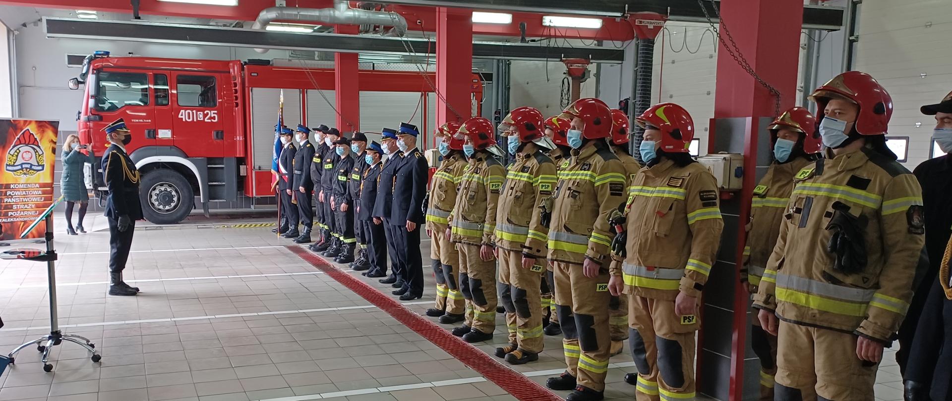 Zdjęcie przedstawia strażaków stojących w szeregu podczas zbiórki z okazji wręczenia odznaczeń, stopni służbowych i nagród.