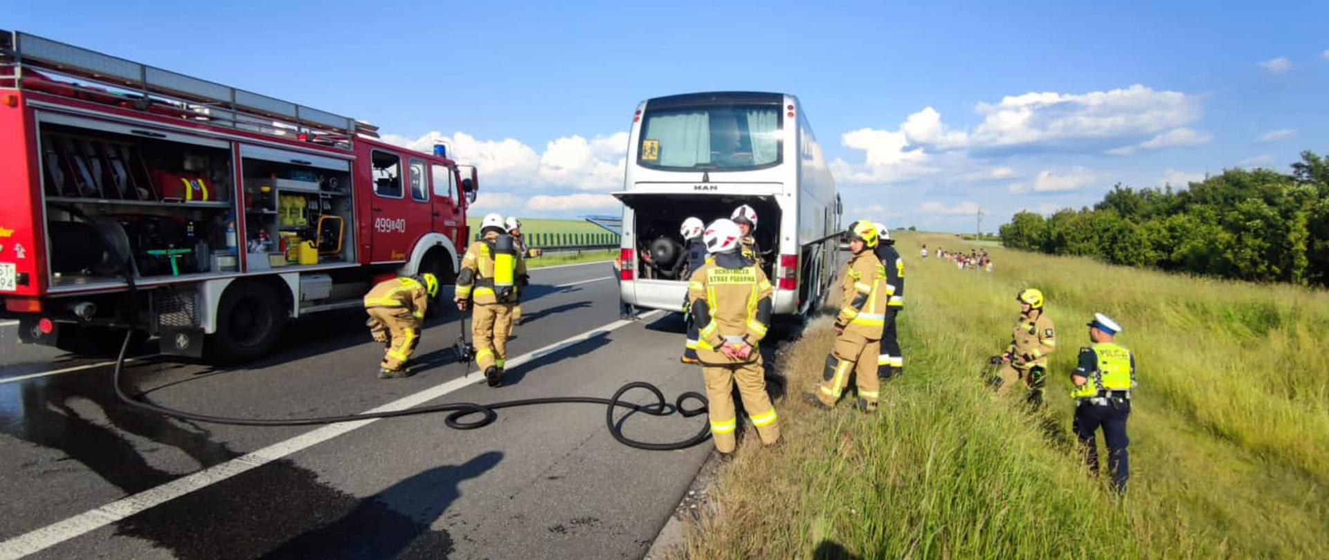 Na zdjęciu znajduje się autokar, wóz strażacki oraz strażacy w ubraniach specjalnych. Pojazdy stoją na autostradzie