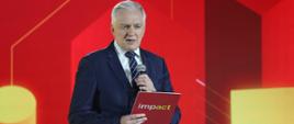 Wicepremier i minister rozwoju, pracy i technologii Jarosław Gowin podczas otwarcia wiosennej edycji Impact"21, z tyłu za jego placami czerwone tło
