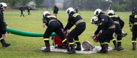 Drużyna męska OSP podczas dobiegnięcia do motopompy, zabierająca sprzęt z podestu.