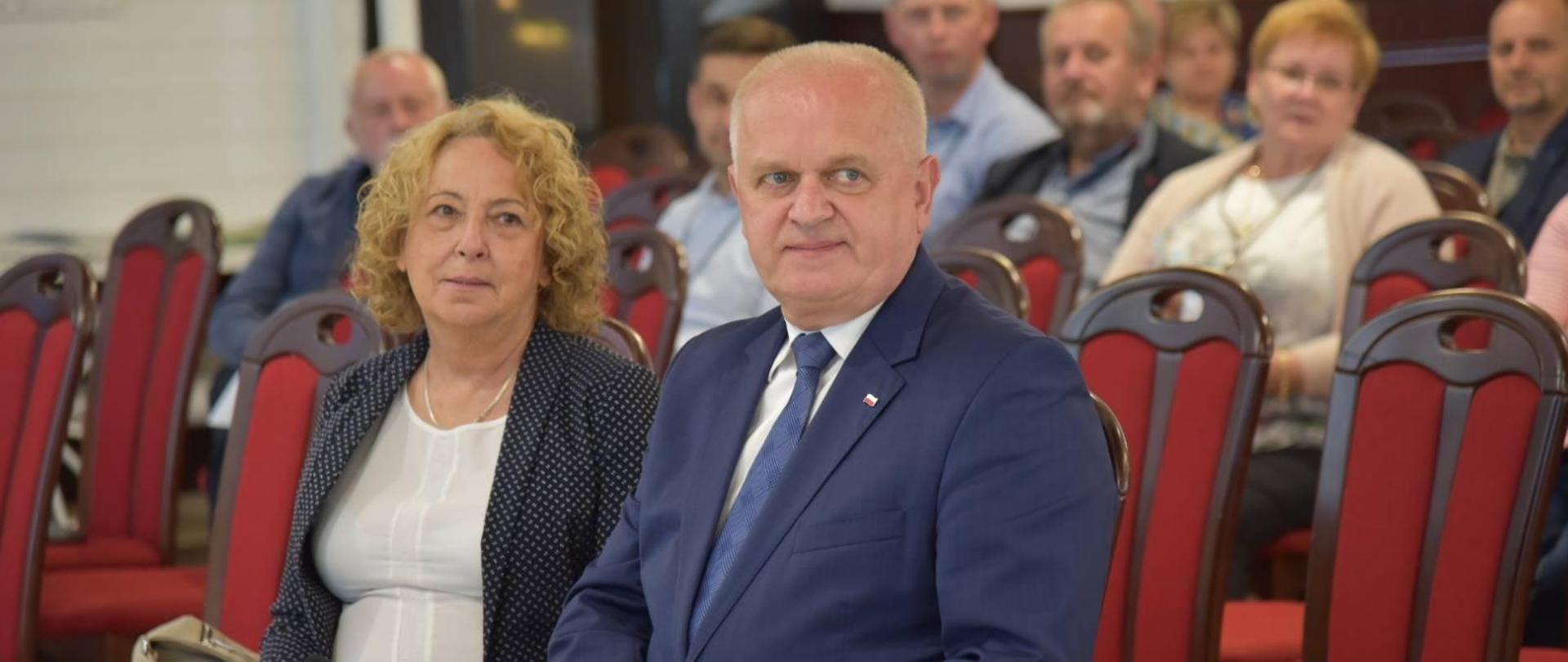 Wojewoda siedzi na krześle,w pierwszym rzędzie przed słuchaczami konferencji