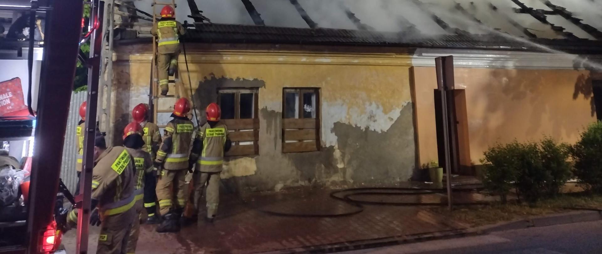 Strażacy prowadzący działania gaśnicze przy pożarze więźby dachowej, która w całości objęta jest pożarem. 