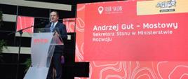 Wiceminister rozwoju i technologii Andrzej Gut-Mostowy przemawiający podczas uroczystego otwarcia TOUR SALON w Poznaniu, wiceminister stoi za mównicą
