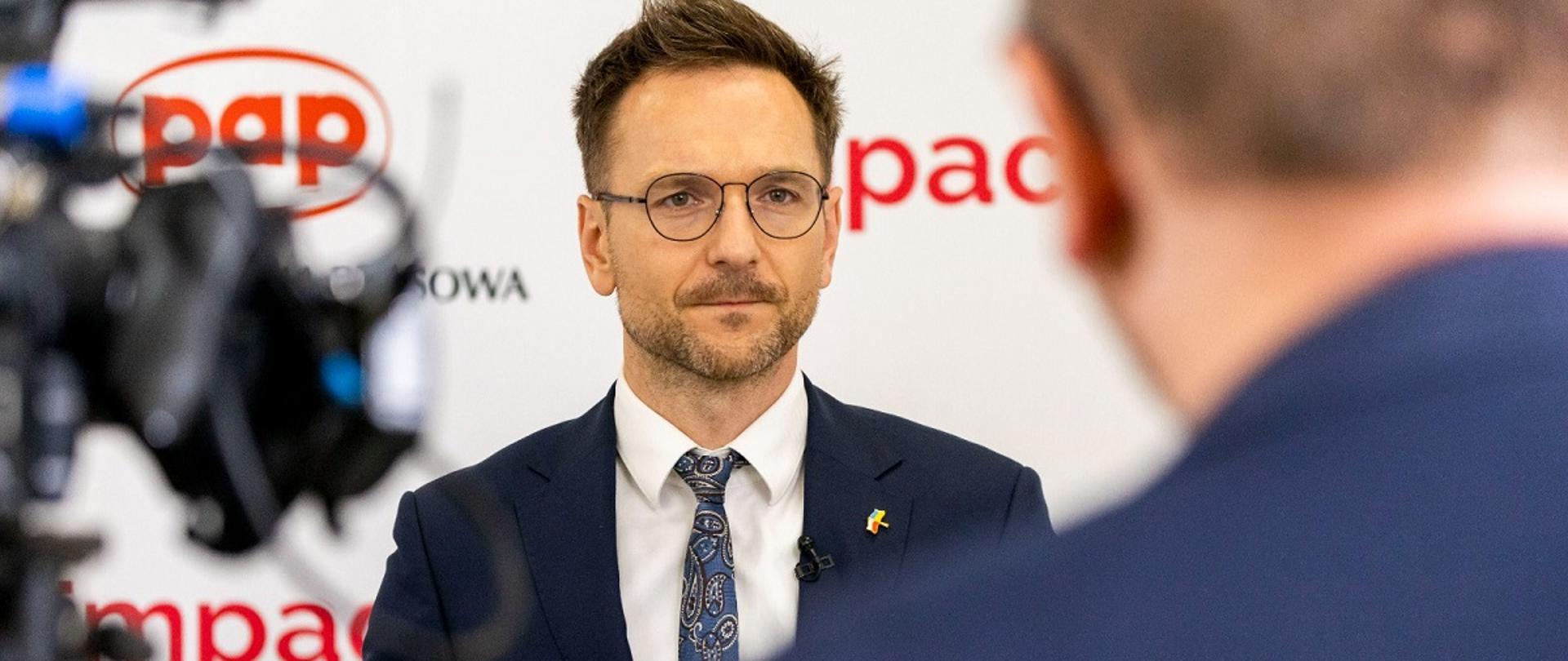 Minister rozwoju i technologii Waldemar Buda udzielający wywiadu podczas Impact'22, za plecami ministra baner z Impact'22 i logo PAP 