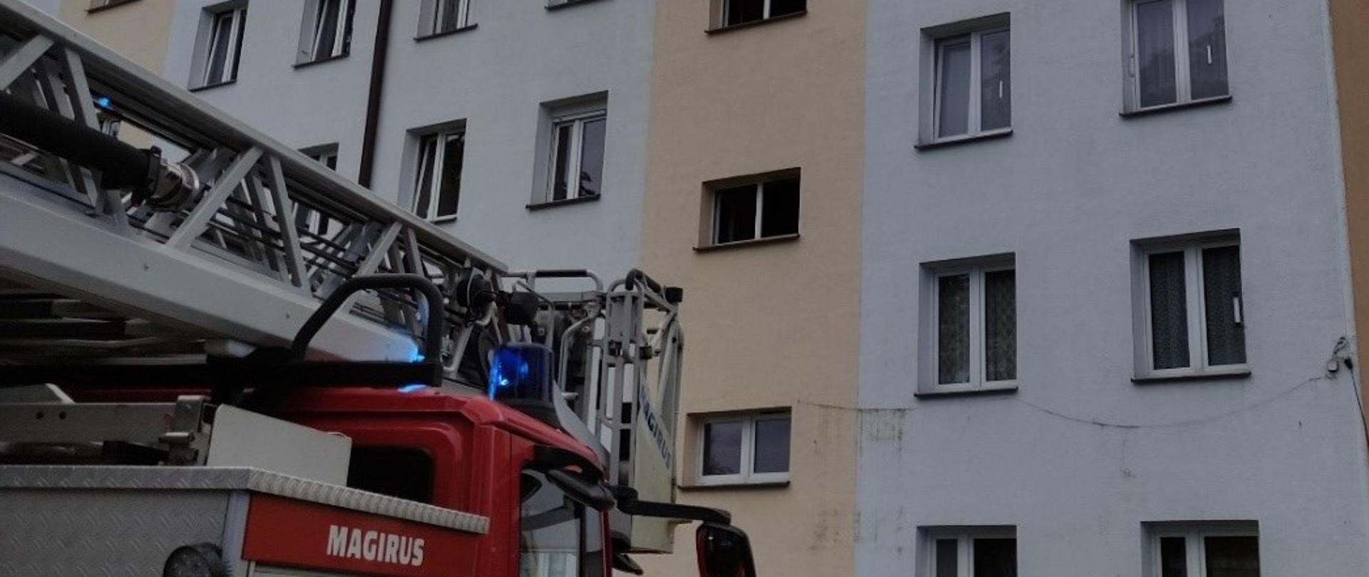 Na zdjęciu samochód pożarniczy - drabina po zakończonych działaniach ratowniczo-gaśniczych. W tle wozu strażackiego blok mieszkalny, w którym doszło do pożaru na najwyższej kondygnacji. 