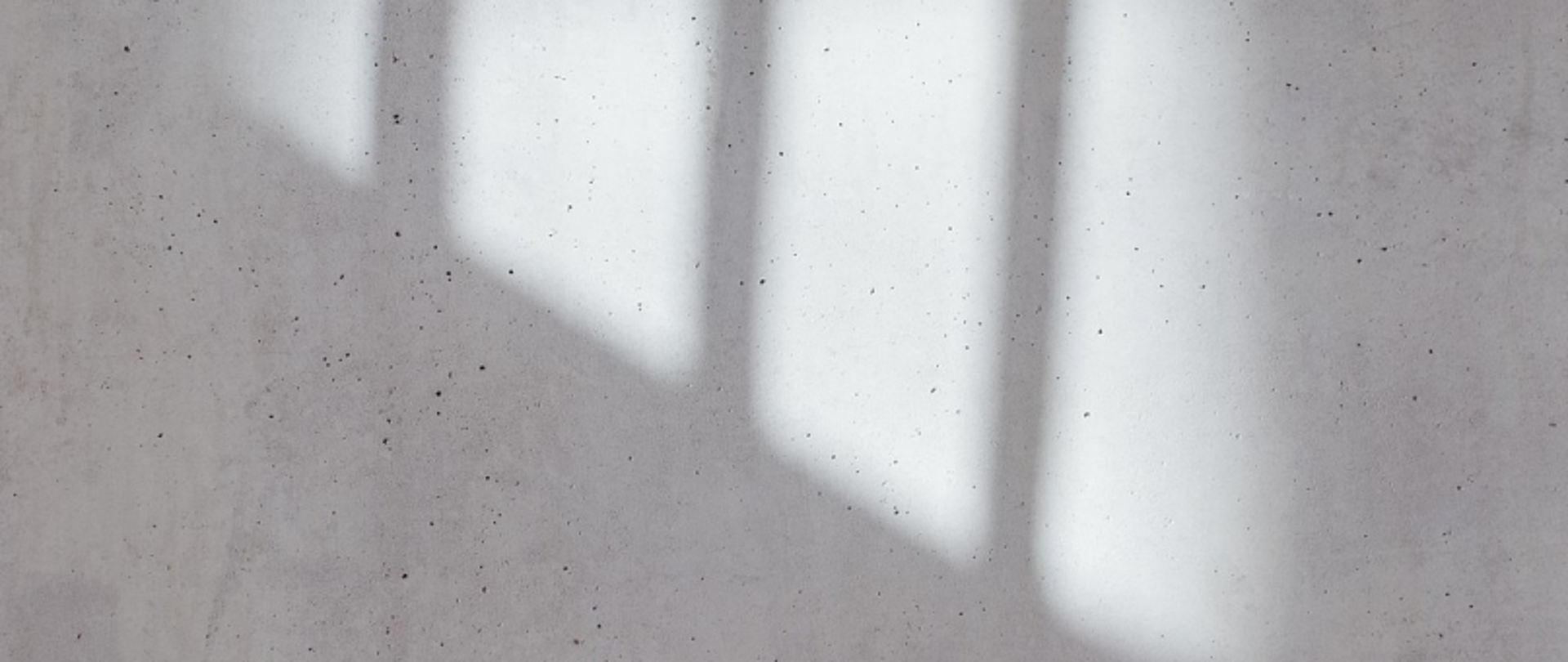 Cienie prostokątnych kształtów na betonowej ścianie, prawdopodobnie rzucane przez okno.