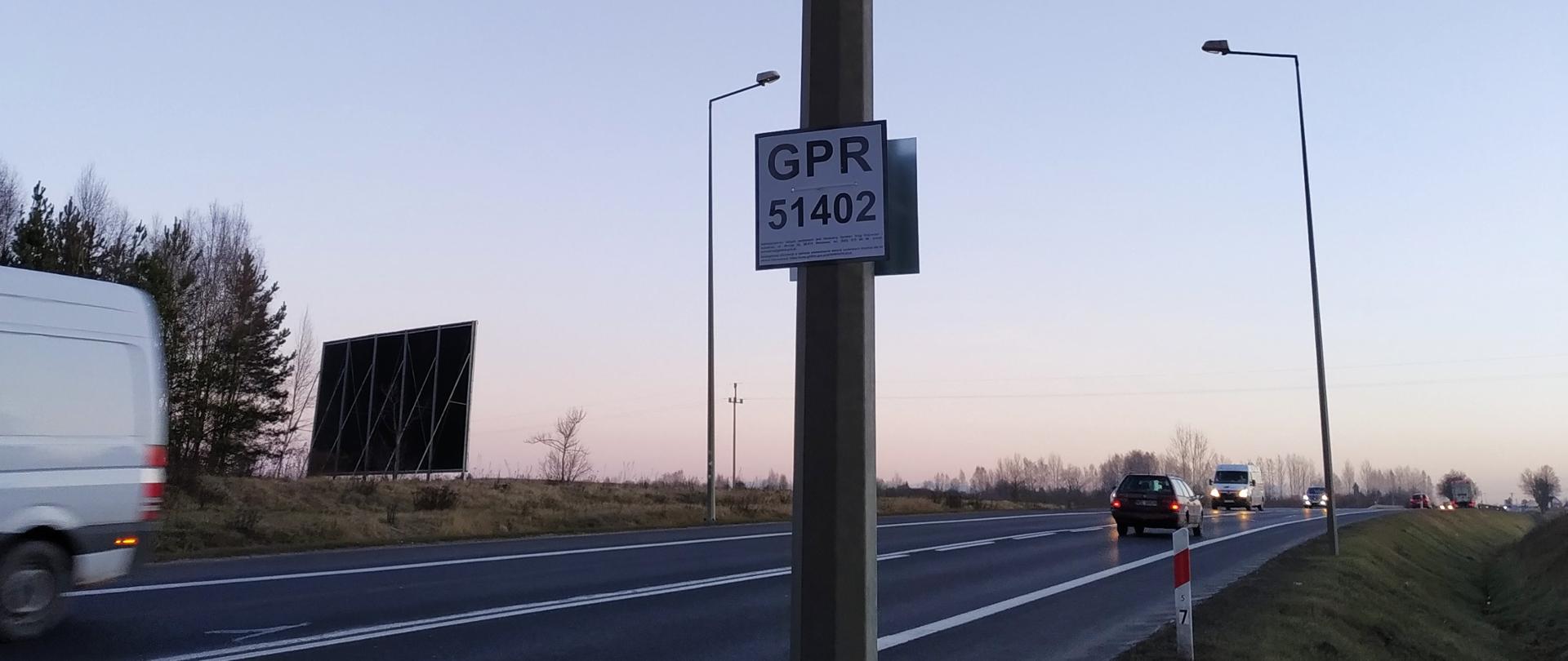 Na zdjęciu widać drogę i jadące po niej auta. W tle widać zachód słońca.