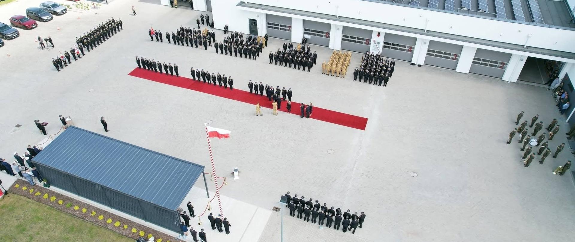 Widok z lotu ptaka na plac Komendy Miejskiej PSP w Grudziądzu podczas uroczystego apelu. Na placu ustawione są pododdziały strażaków, poczty sztandarowe oraz uczestnicy obchodów Dnia Strażaka.