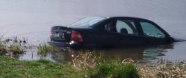 na nabrzerzu rzecznym widać auto częściowo zanurzone w wodzie.