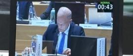 Widać ekran przedstawiający mężczyznę w sali konferencyjnej