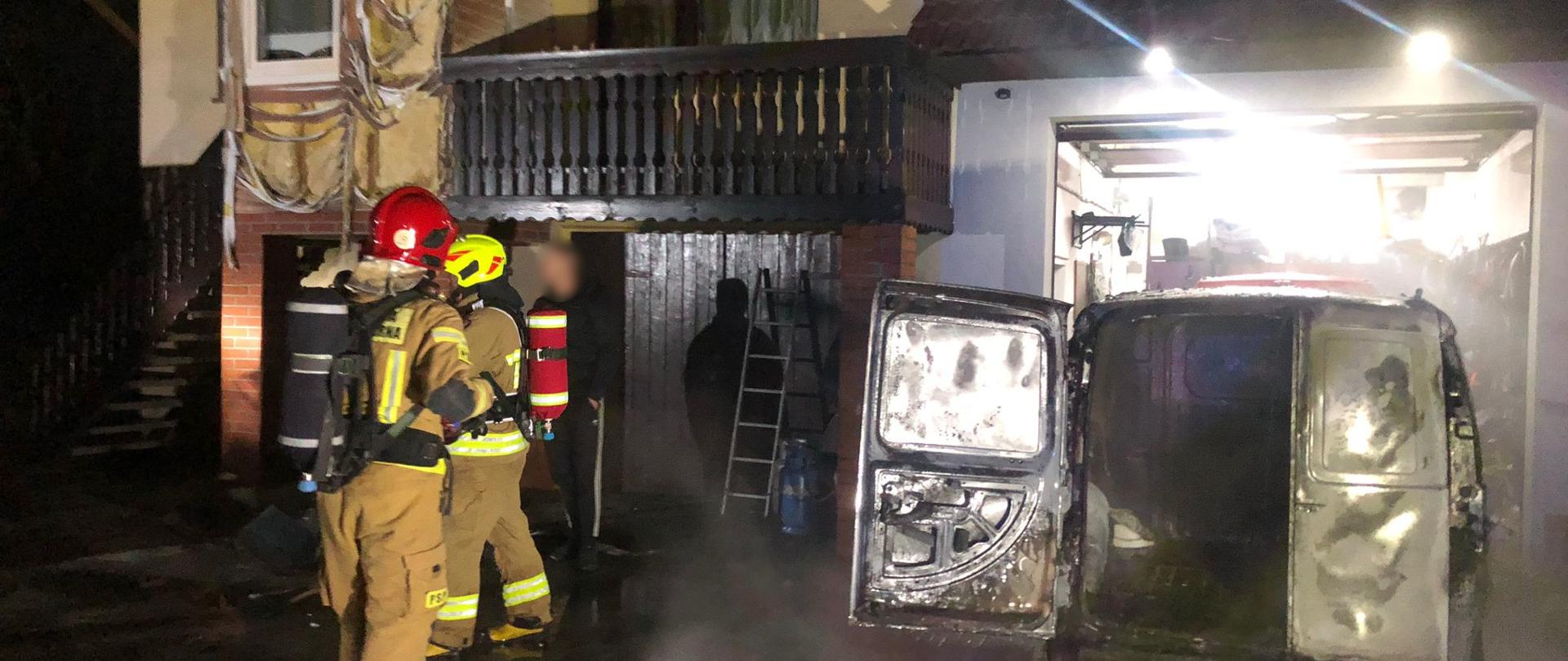 Widoczne miejsce zdarzenia uszkodzone budynki, pojazdy oraz strażacy podczas działań.