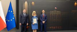Trzy osoby stoją na ściance Urząd Skarbowy Przyjazny Przedsiębiorcy. Kobieta trzyma dyplom.
