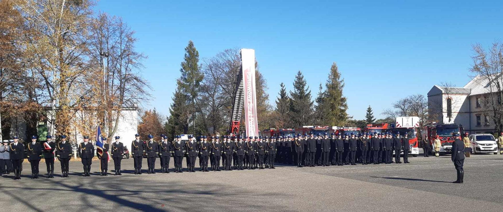 Kompanie gotowe do uroczystości. Po lewej stronie poczty: flagowy i sztandarowy. W tle samochody pożarnicze oraz budynki Centralnej Szkoły Państwowej Straży Pożarnej w Częstochowie