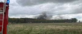 W oddali widać i unoszą cy się czarny dym. Z lewej strony fragment tyłu pojazdu strażackiego. Pochmurnie.