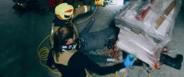 Zdjęcie przedstawia strażaków podczas ćwiczeń udzielających pomocy osobie przygniecionej pod paletą.