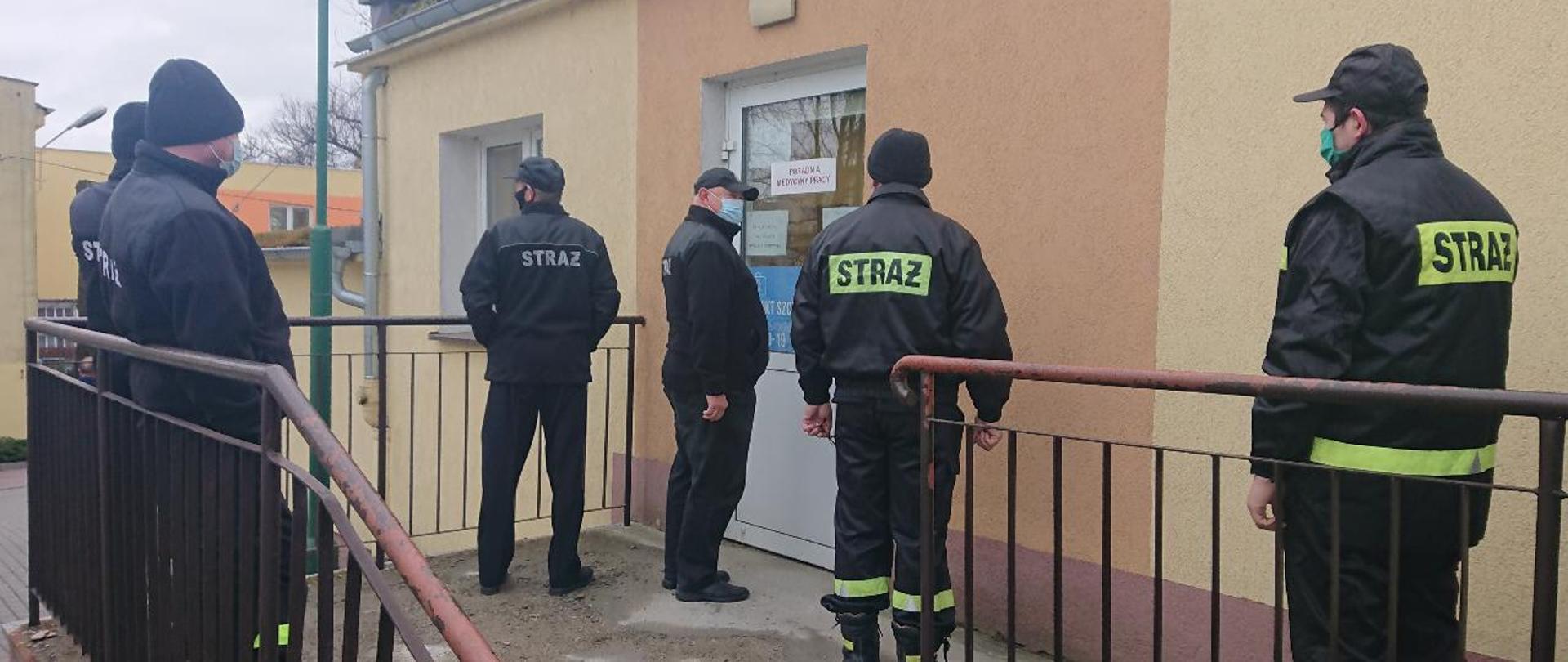 zdjęcie przedstawia grupę strażaków stojących przed punktem szczepień 