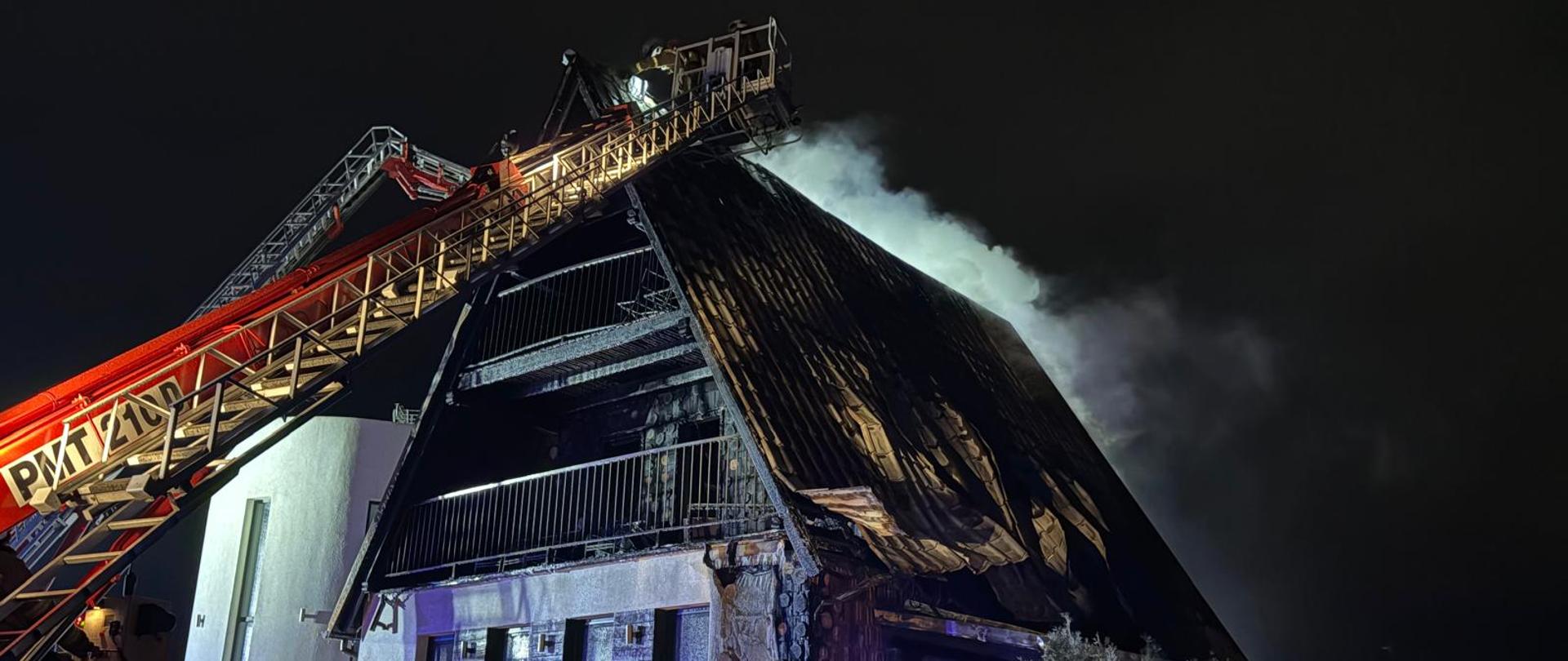 Strażacy gaszą z drabiny pożarnicze dach palącego się hotelu.