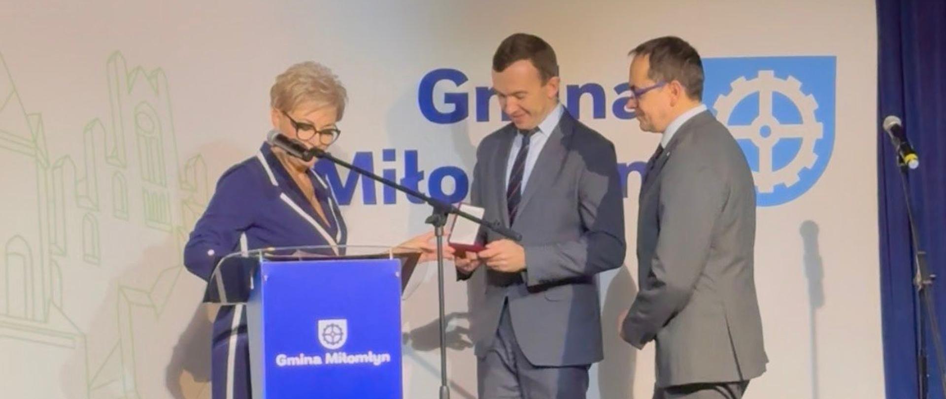 Dwóch mężczyzn i kobieta na scenie za mównicą