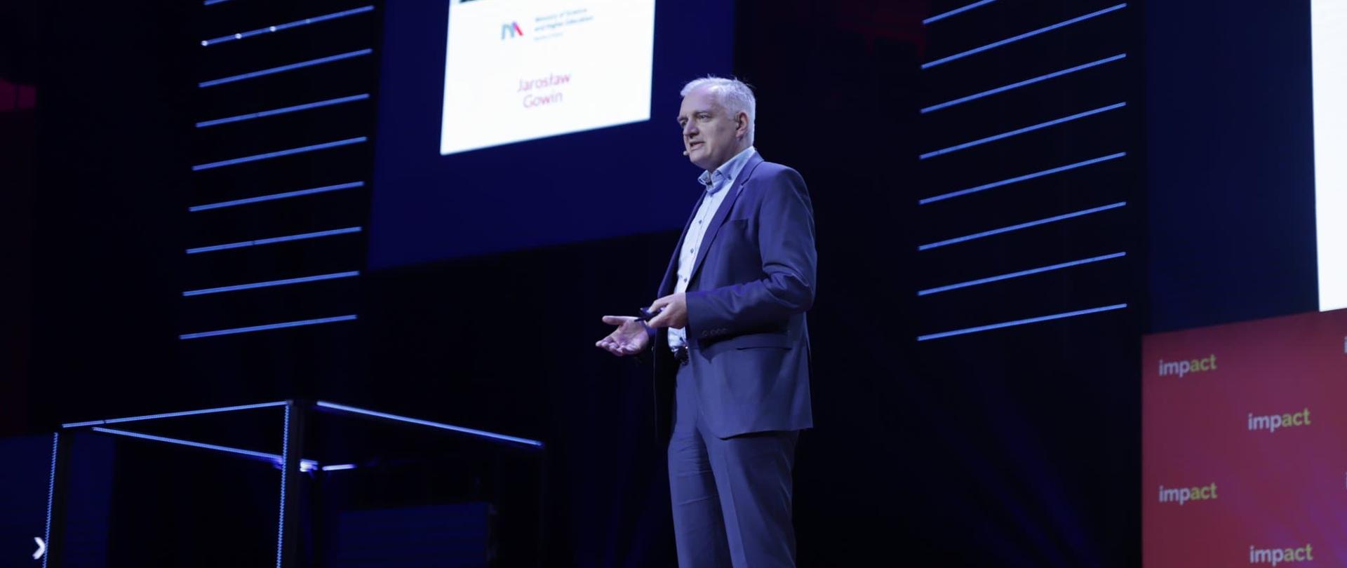 Minister Gowin przemawia do mikrofonu na tle ciemnej ściany