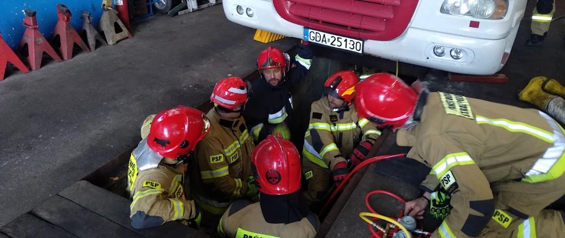 Strażacy Państwowej Straży Pożarnej ćwiczą wydobycie mechanika, którego przygniótł naprawiany pojazd ciężarowy.