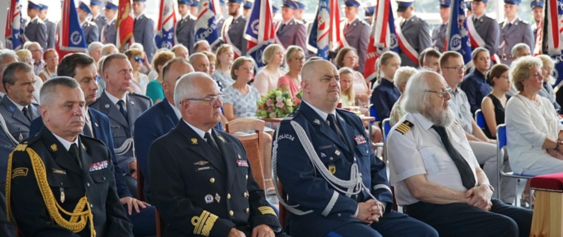 Przedstawiciele służb mundurowych oraz zaproszeni goście siedzą na krzesłach podczas uroczystości.