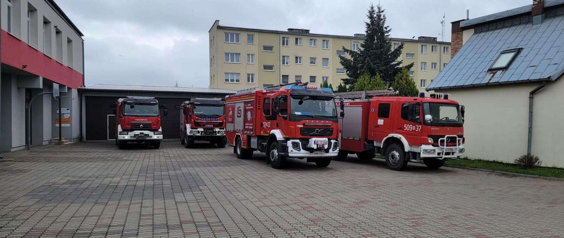 Na zdjęciu widać budynki oraz pośrodku plac na którym soją cztery wozy strażackie. 