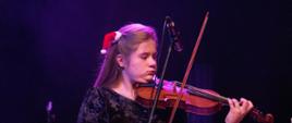 Zdjęcie przedstawia uczennicę Marię Silińską grającą na skrzypcach na scenie podczas koncertu świątecznego.