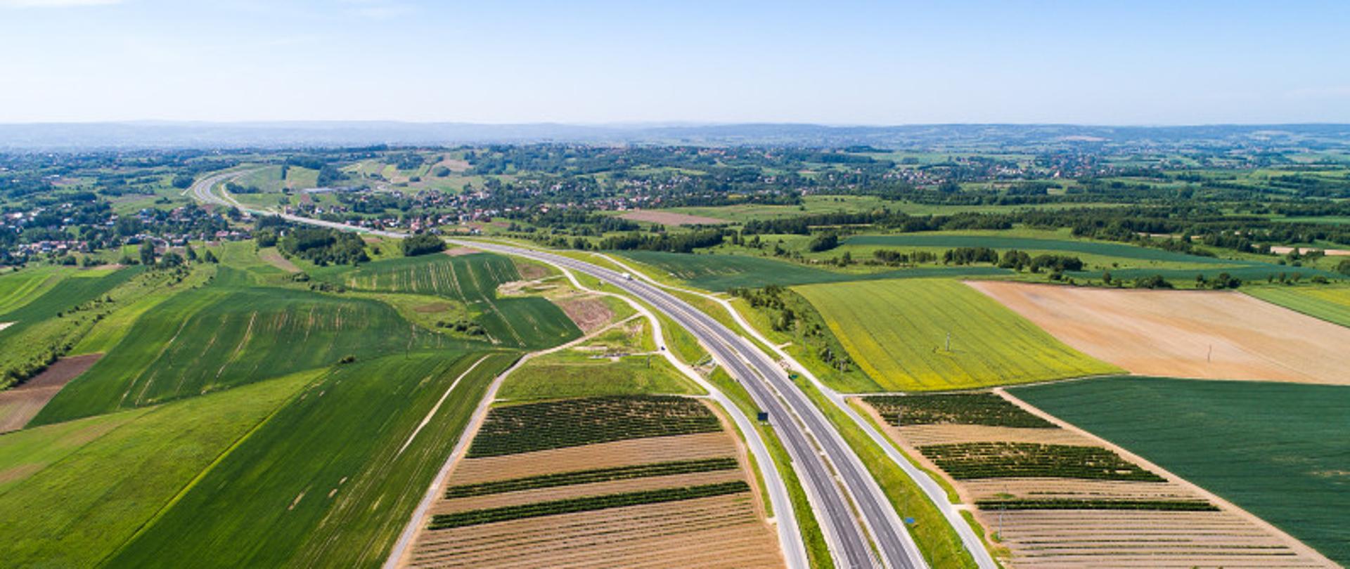Widok z góry na dwujezdniową drogę biegnącą wśród pól i łąk 