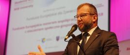 Minister funduszy i polityki regionalnej Grzegorz Puda na konferencji poświęconej funduszom europejskim na Akademii Wyższej Szkoły Biznesu w Żywcu, minister stoi przy mównicy i przemawia do mikrofonu