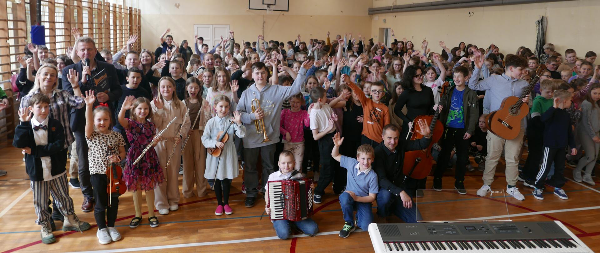 Na zdjęciu widzimy zarówno uczniów ze szkoły muzycznej trzymających instrumenty jak dzieci i młodzież ze szkoły podstawowej która przyszła na koncert.